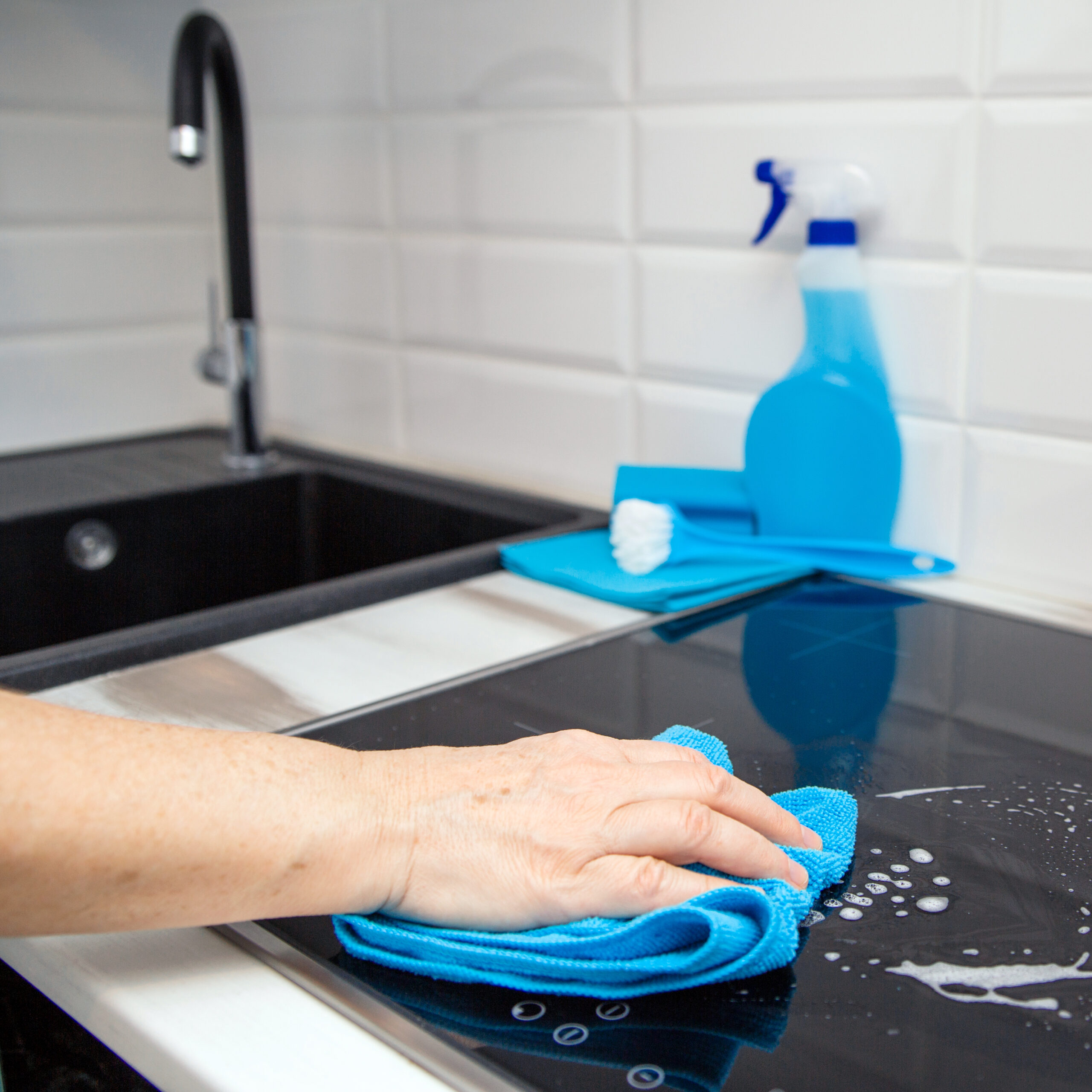 woman s hand with blue microfibre cloth rubs glass ceramic plate kitchen